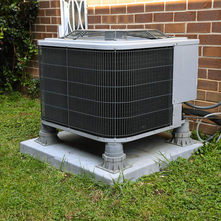 Outdoor air conditioning unit on a concrete pad next to a brick house.